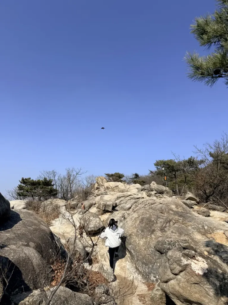 Hiker in white jacket descending rocky trail on Hoamsan Mountain Seoul