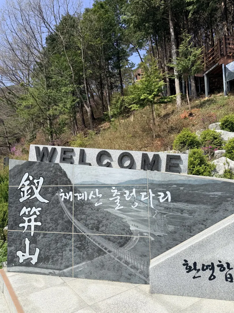 Welcome sign at Chaegyesan hiking trail entrance with suspension bridge image