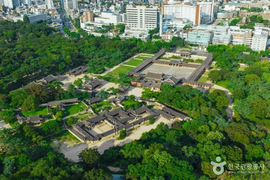 Aerial view of Changgyeonggung Palace surrounded by dense forest and Seoul buildings