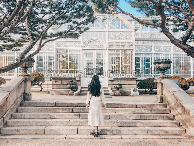 Woman descending stone steps toward glass greenhouse at Changgyeonggung Palace