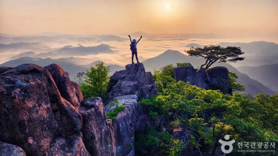 Hiker celebrates sunrise atop Daedunsan mountain peaks with layered valleys below