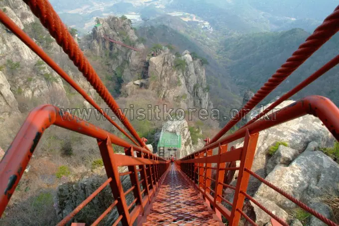 Red suspension bridge with three-line stairs spanning dramatic mountain valley