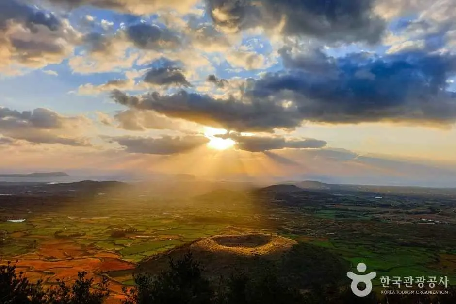 Golden sunrise breaking through clouds over Darangshi Oreum crater landscape
