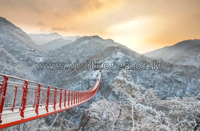 Red suspension bridge at sunrise over snowy Gamaksan mountains