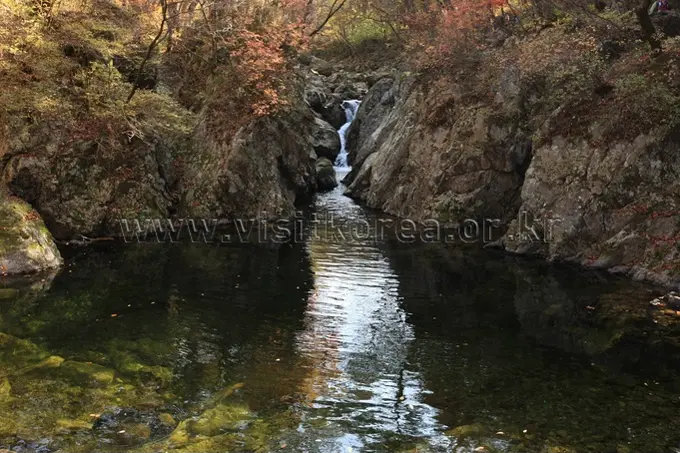 Guryongso waterfall cascade flowing into emerald pool surrounded by moss-covered rock canyon