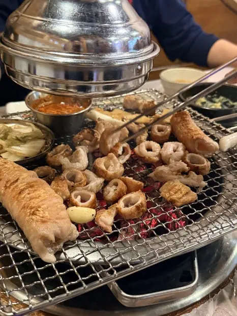 Grilled pork makchang and offal on Korean BBQ grill with dipping sauces