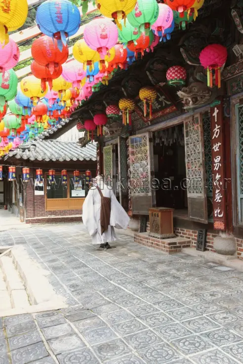 Monk in white robes at Sojae-am temple courtyard with colorful lanterns