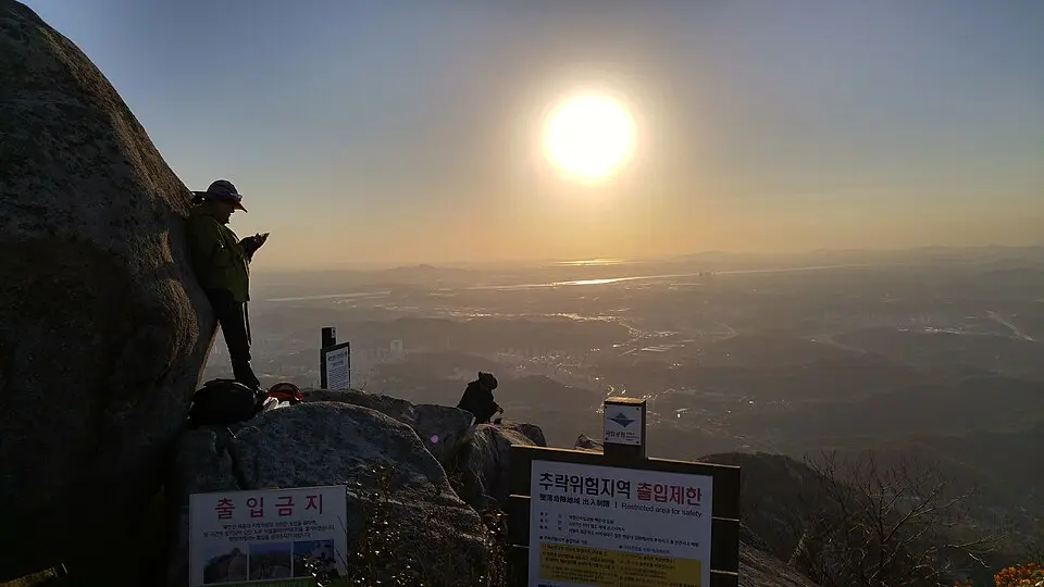Hikers at Baegundae peak summit at sunset with panoramic valley view