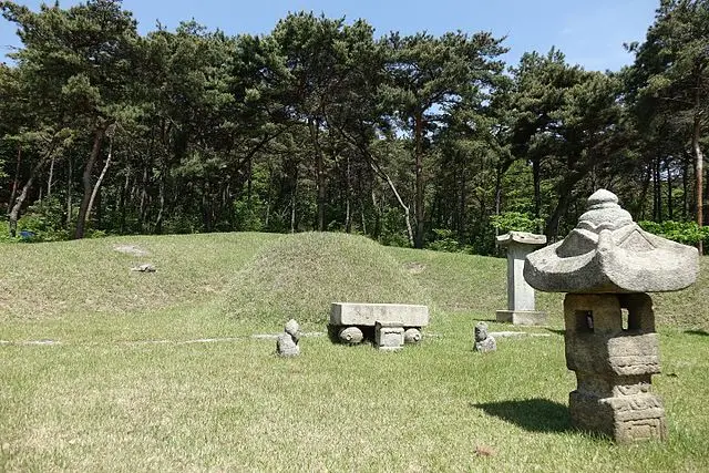 Stone lantern monument in grassy cemetery clearing surrounded by forest trees