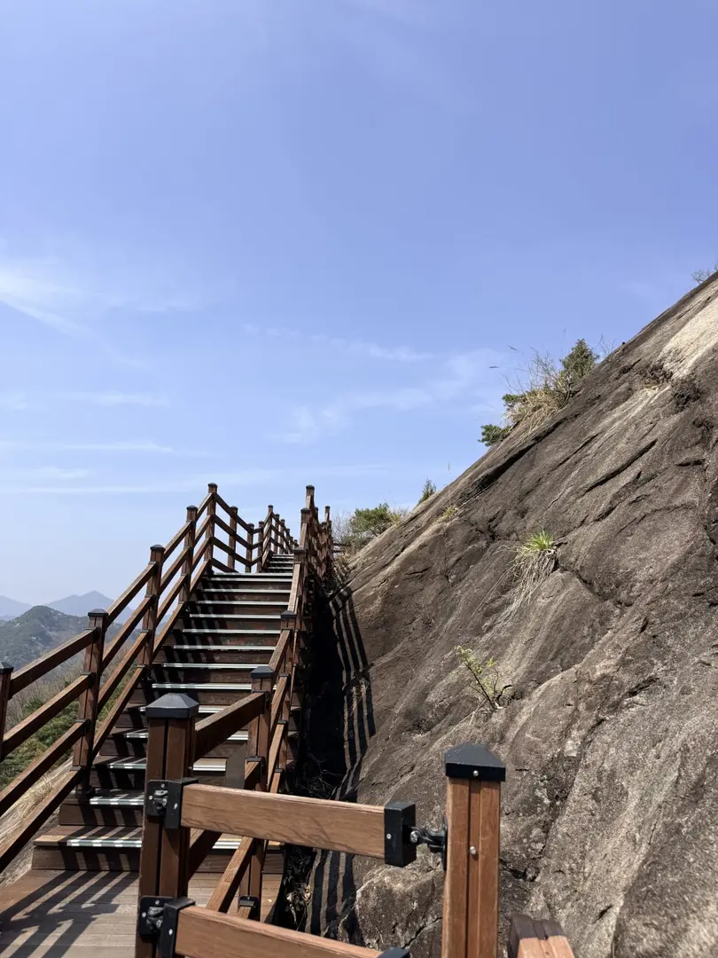 Steep wooden staircase climbing along rocky cliff face on Korean hiking trail