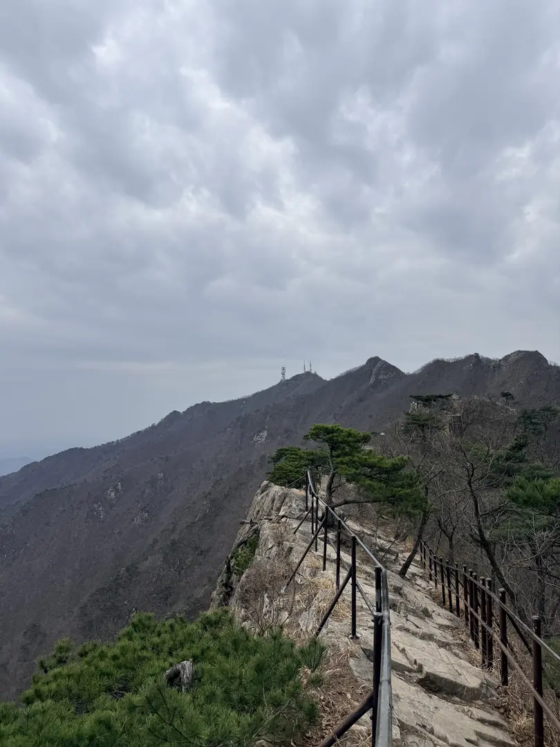 Wooden safety railing along steep mountain ridge trail with forested peaks