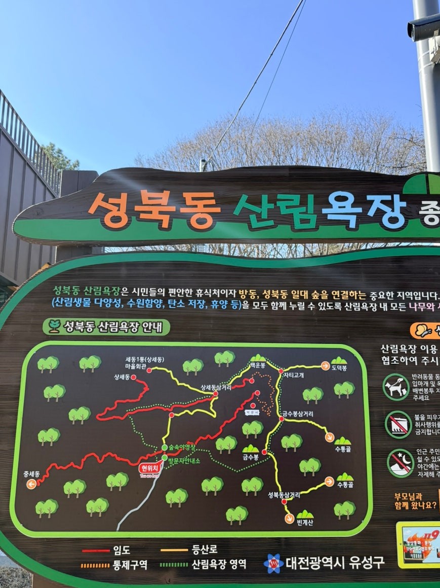 Trailhead information board at Seongbuk-dong Forest Bathing Area showing a color-coded trail map with red, yellow, and green route markings through the hills of Yuseong-gu, Daejeon, with Korean guidelines listed on the right panel