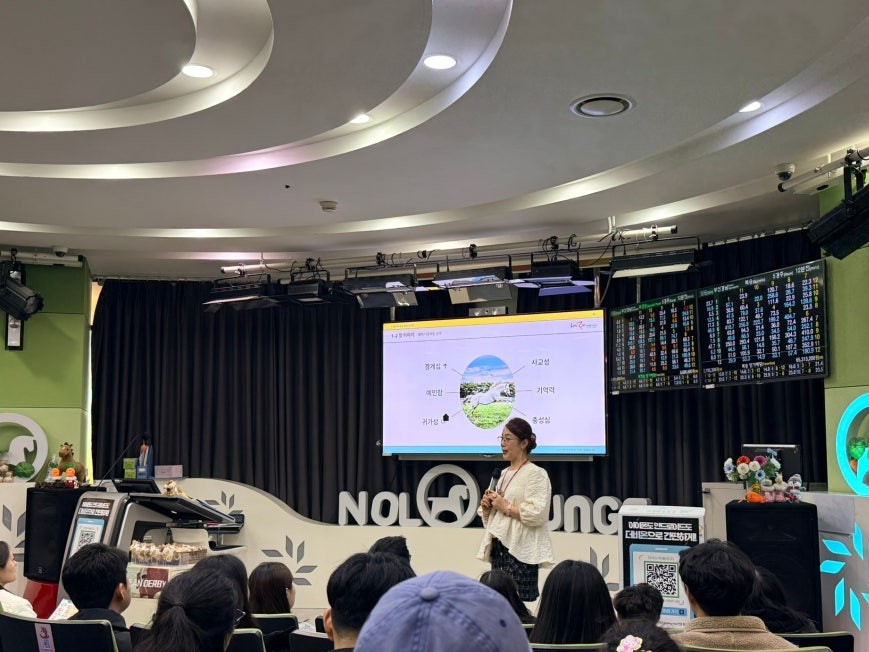 Beginner's Class session at Let's Run Park Seoul with a presenter holding a microphone at the front, audience seated in rows, projection screen showing horse racing concepts, and race odds displays on side walls