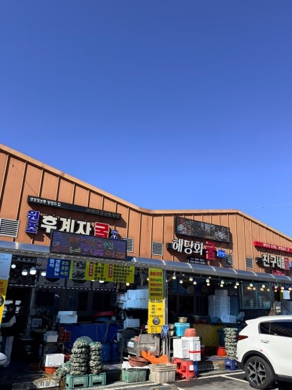 Row of three seafood restaurants side by side at Cheonbuk Oyster Village — 후계자굴, 해당화굴, and 친구네굴 — with colorful signage under a clear blue winter sky