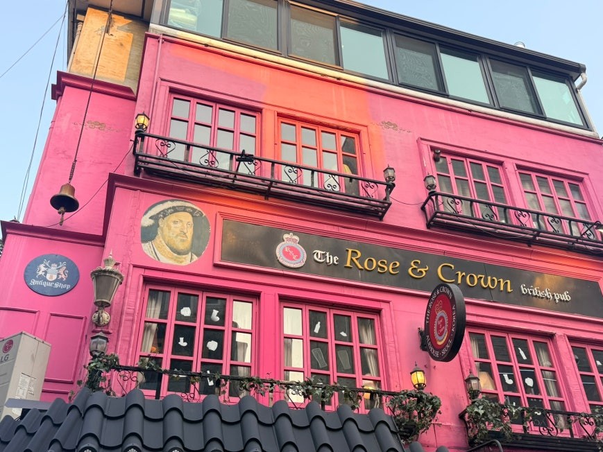 Bright pink three-story exterior of The Rose & Crown British Pub in Itaewon with Tudor portrait panels, wrought iron balconies, and pub signage