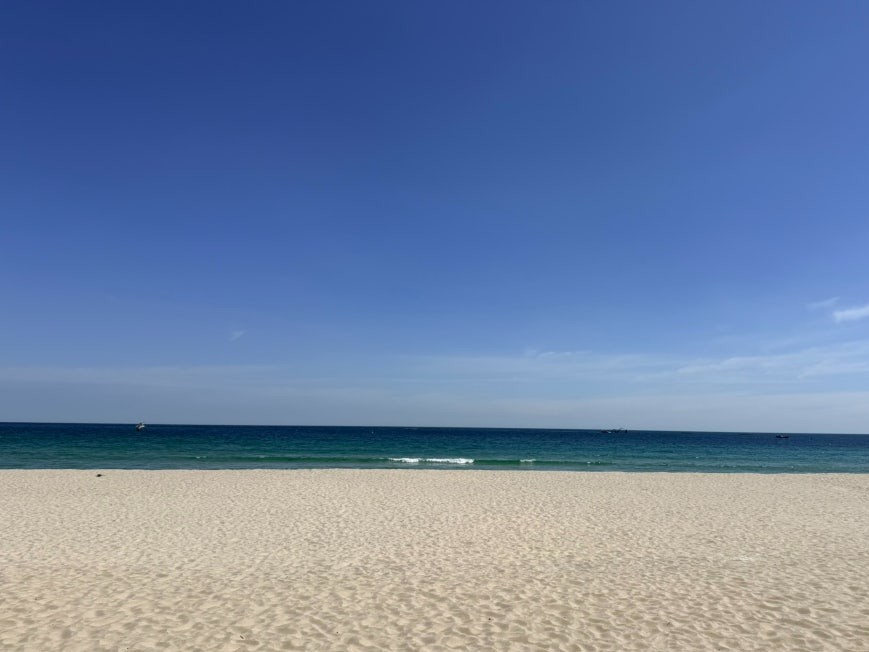 Wide empty white-sand beach stretching to a calm turquoise East Sea horizon under a cloudless blue sky near Yonghwa Station