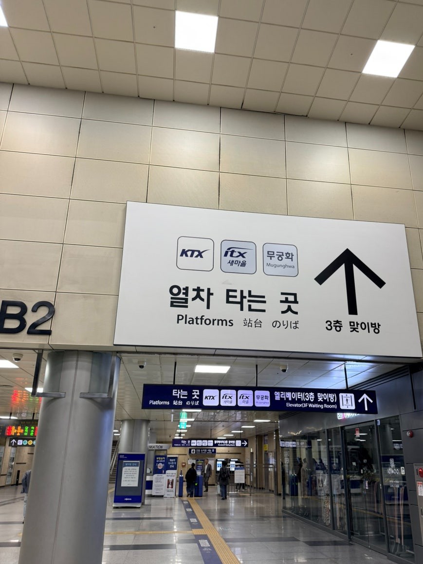 Bilingual platform wayfinding sign at Cheongnyangni Station showing KTX, ITX-Saemaeul, and Mugunghwa train service icons with a large directional arrow pointing toward the platforms, labeled in Korean, English, and Japanese, with the B2 concourse column visible on the left