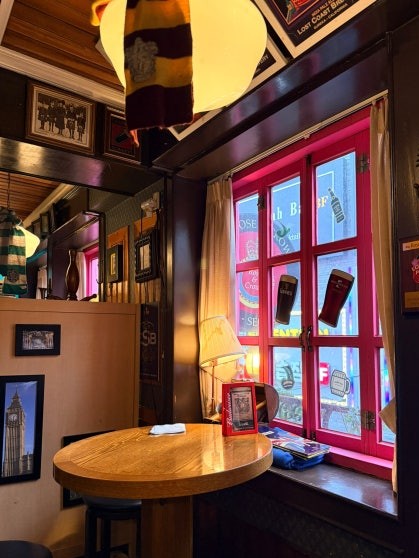 Corner table at Rose & Crown Itaewon with bright red window frames, a Harry Potter-style striped scarf hanging above, and a Big Ben photo on the dark wood wall