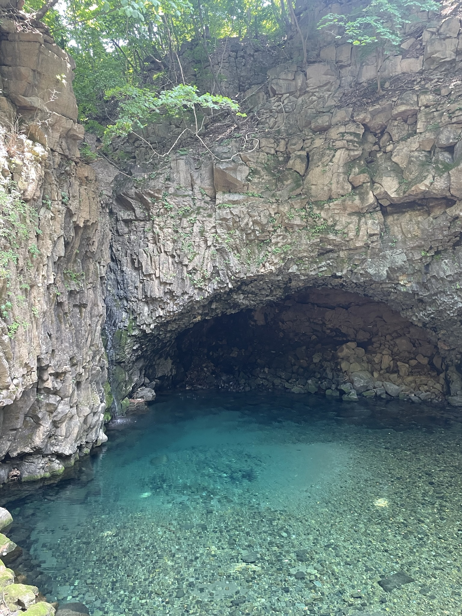 Turquoise natural pool filling the floor of a rocky cave chamber, fractured rock walls and pebble bed visible through exceptionally clear water, Pocheon, South Korea